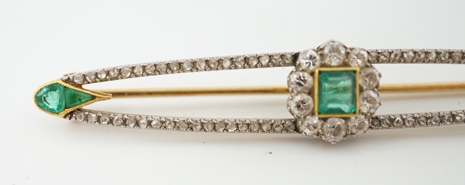 A Belle Epoque gold and platinum, emerald and round cut diamond cluster set elliptical bar brooch